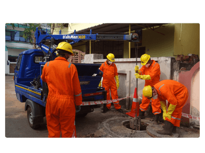 Sanitation workers in orange PPE operating mechanized desludging equipment at a manhole